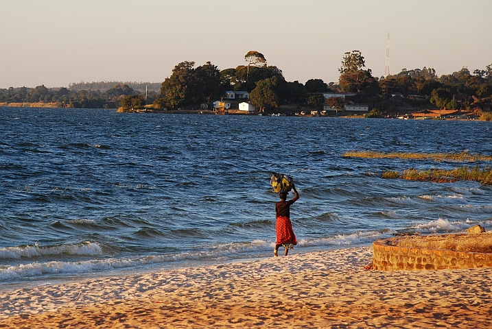 Lastentragende Frau unterwegs am Strand von Samfya