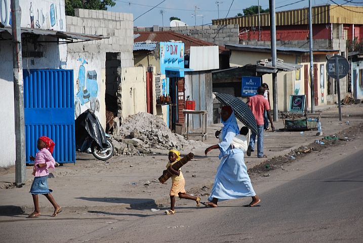 Frau mit Schirm und Kinder gut geschützt vor der Sonne unterwegs in einem Vorort von Brazzaville